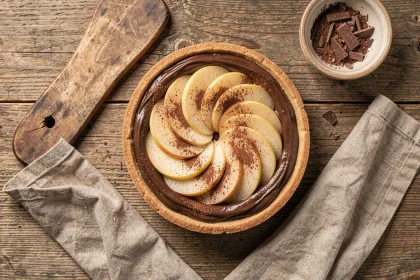 Tarte poire chocolat vue de dessus sur table en bois avec napkin lin et copeaux de chocolat